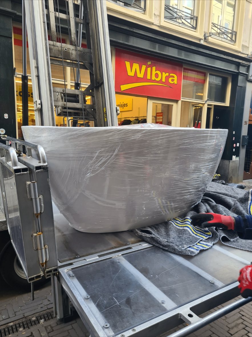 Vrijstaand ligbad ingepakt in folie op de verhuislift van de bakwagen in een winkelstraat