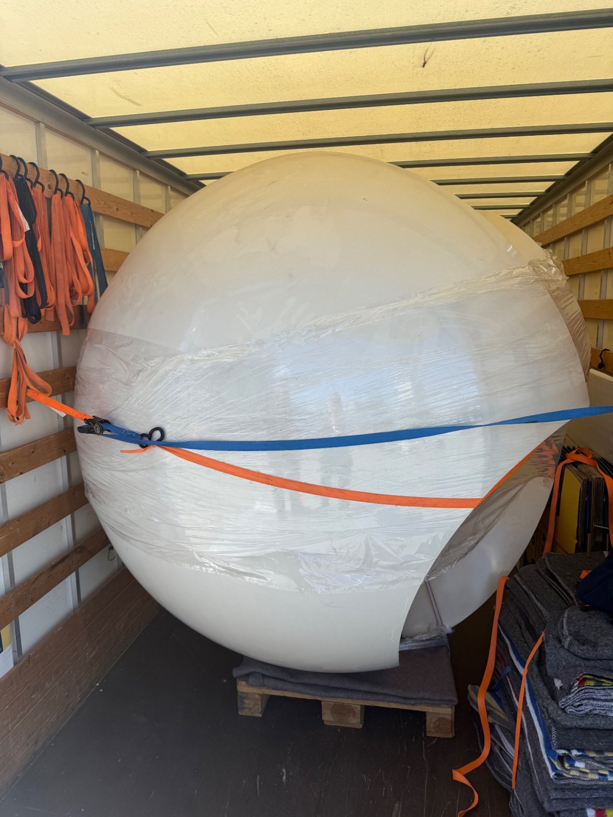 Grote witte decoratiebol ingepakt in folie en vastgezet met spanbanden in de bakwagen