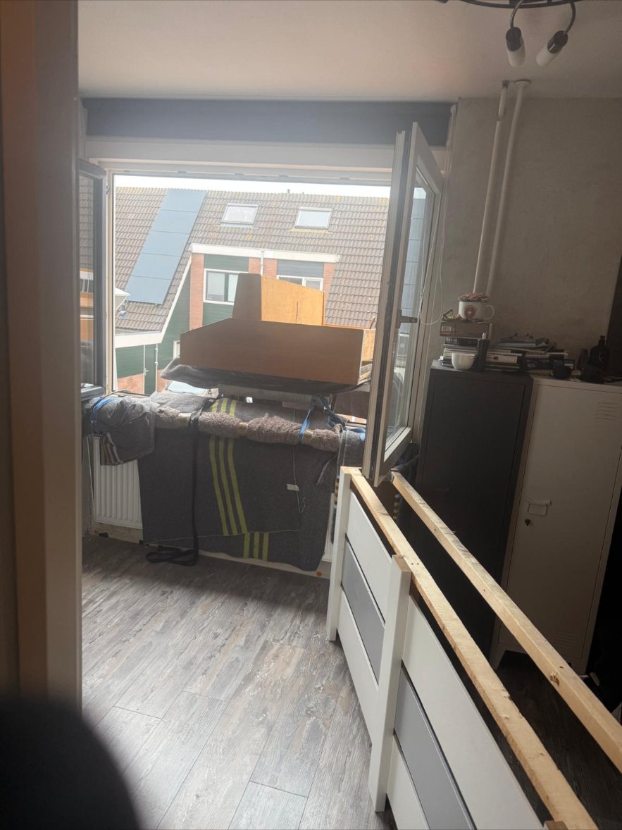 Piano ingepakt in verhuisdekens en met spanbanden klaar om via het balkon van een bovenwoning naar buiten te gaan