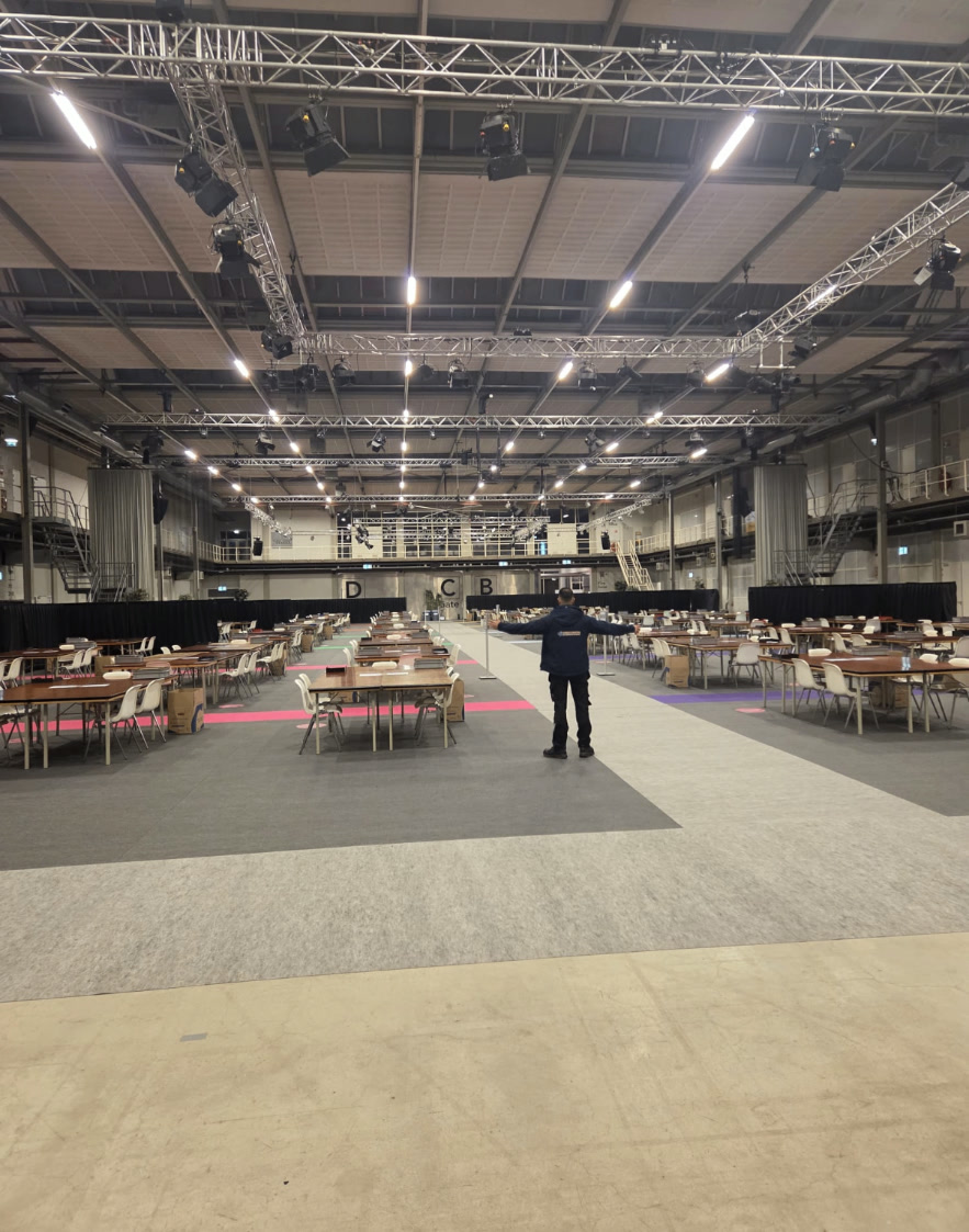 Grote evenementenhal met tafels, stoelen en tapijtbanen klaar voor gebruik